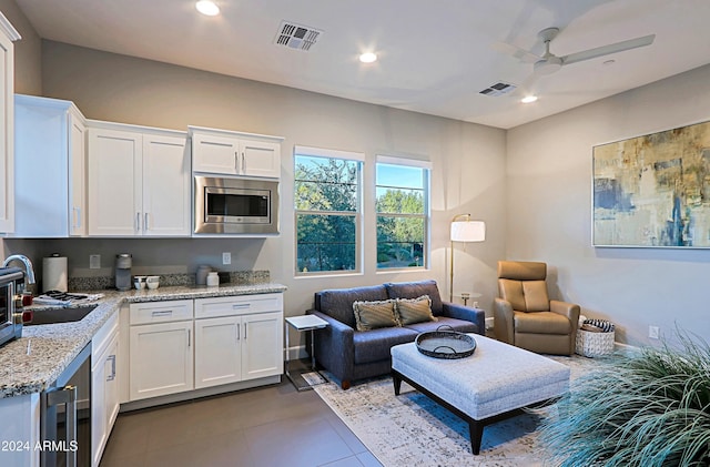 kitchen with white cabinetry, stainless steel microwave, ceiling fan, sink, and light stone counters