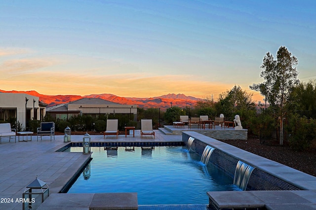 pool at dusk with a mountain view, pool water feature, and a patio