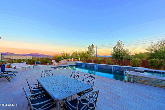 pool at dusk featuring pool water feature, a mountain view, an in ground hot tub, and a patio