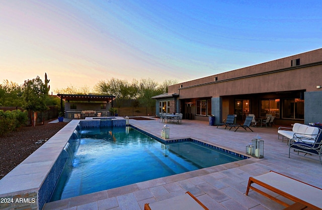 pool at dusk with pool water feature and a patio area