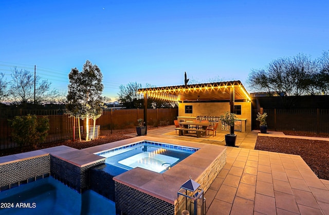 pool at dusk with a patio area and an in ground hot tub