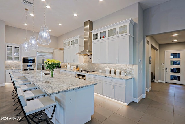 kitchen featuring built in appliances, white cabinetry, a spacious island, and wall chimney range hood