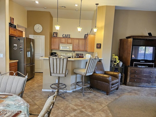 kitchen featuring a towering ceiling, decorative light fixtures, a breakfast bar area, kitchen peninsula, and white appliances