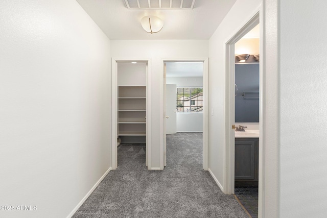 hallway with baseboards, a sink, dark colored carpet, and visible vents