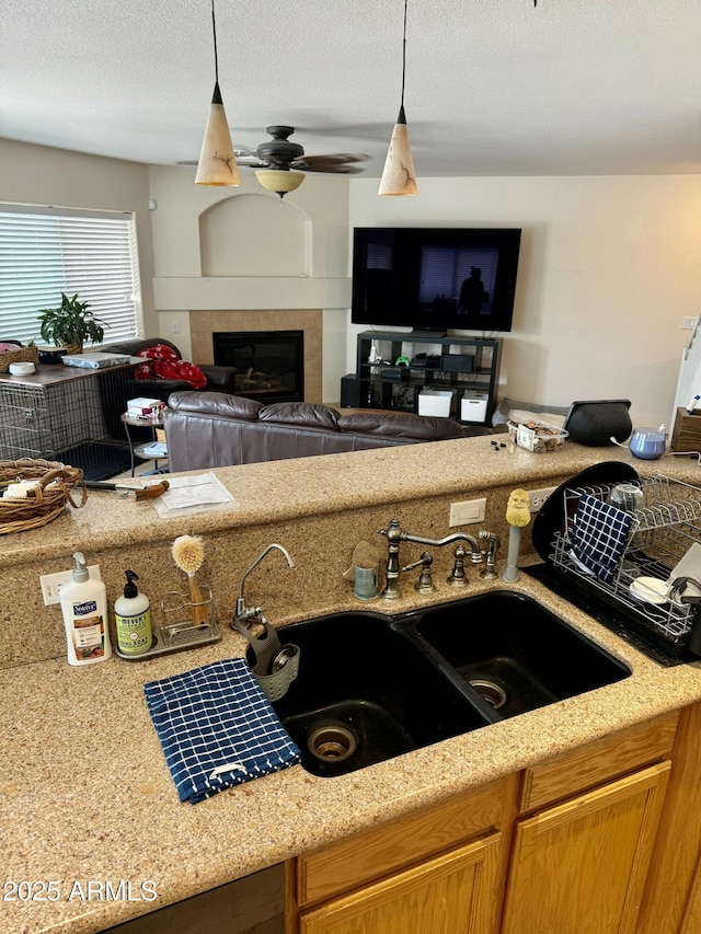 kitchen with a tile fireplace, pendant lighting, a sink, and ceiling fan