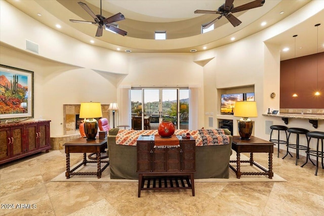 living room featuring ceiling fan, a high ceiling, and a tile fireplace