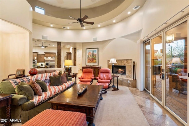 living room with a wealth of natural light, a tiled fireplace, ceiling fan, and a high ceiling