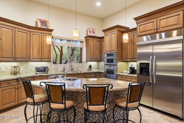 kitchen with stainless steel appliances, hanging light fixtures, a center island with sink, and light stone counters