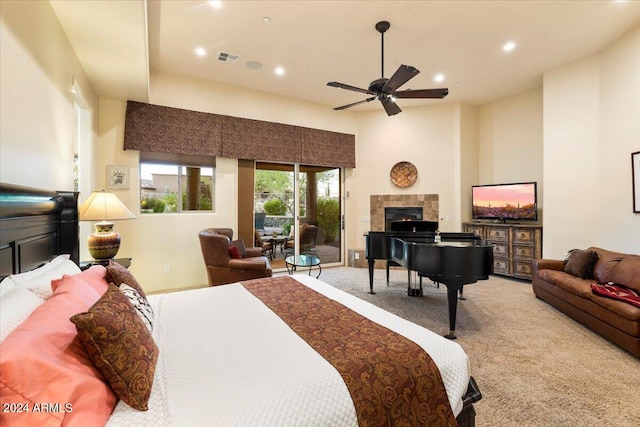 carpeted bedroom featuring access to exterior, a towering ceiling, a tiled fireplace, and ceiling fan