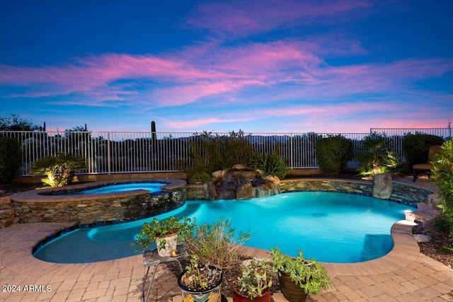 pool at dusk with pool water feature and an in ground hot tub