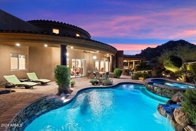 pool at dusk featuring ceiling fan, an in ground hot tub, and a patio area