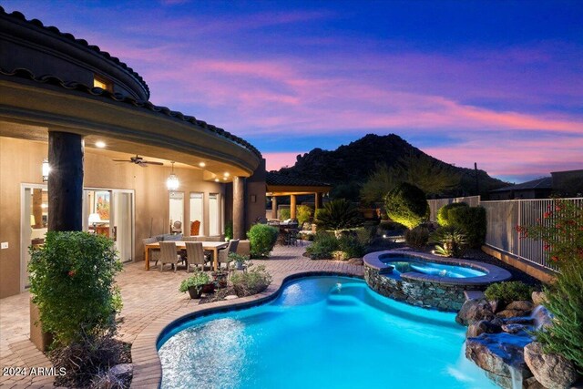 pool at dusk featuring ceiling fan, a patio, and an in ground hot tub