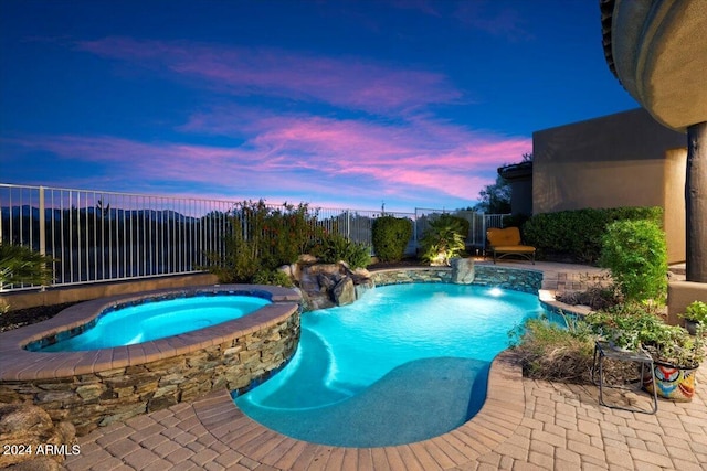 pool at dusk with an in ground hot tub, pool water feature, and a patio area