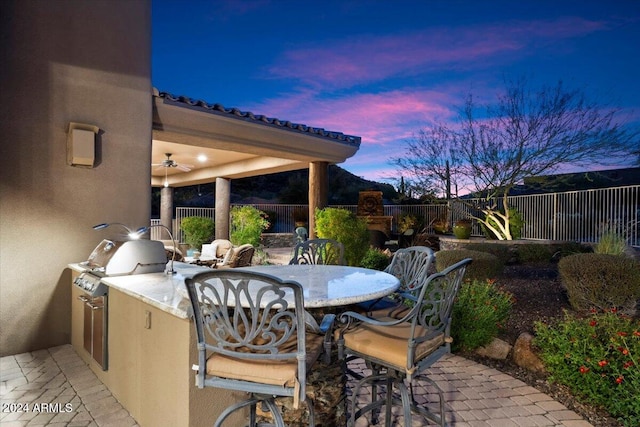 patio terrace at dusk with an outdoor kitchen and area for grilling