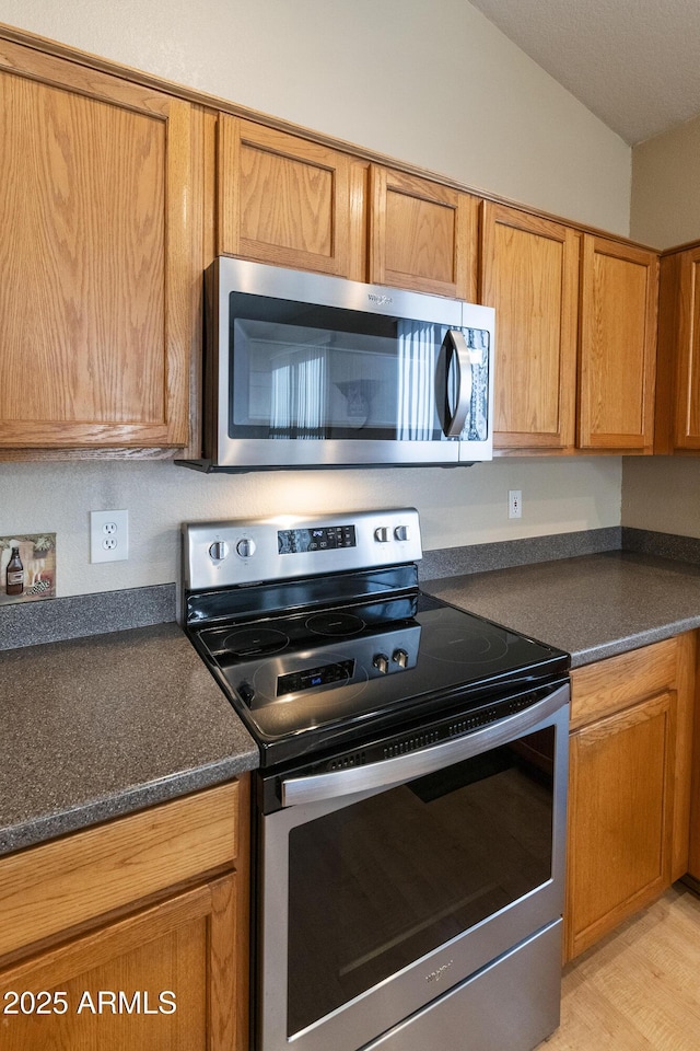 kitchen featuring light wood-type flooring, vaulted ceiling, and appliances with stainless steel finishes