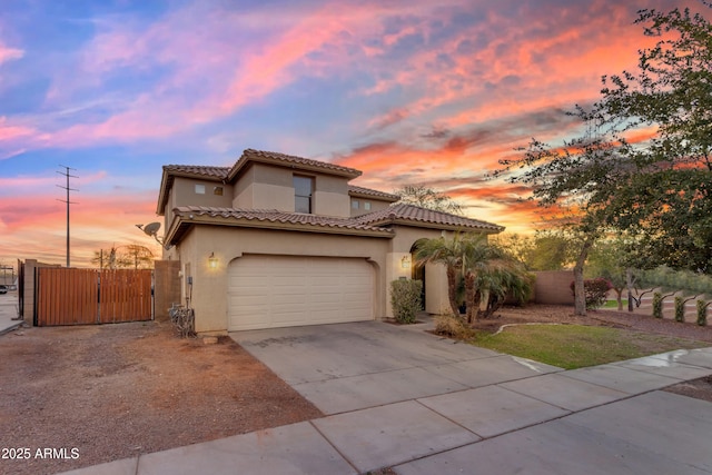 mediterranean / spanish-style home with an attached garage, fence, driveway, a tiled roof, and stucco siding