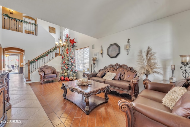 living area featuring arched walkways, a notable chandelier, stairway, a towering ceiling, and wood finished floors