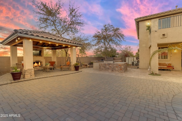 view of patio / terrace with a lit fireplace, a gazebo, exterior kitchen, and a fenced backyard