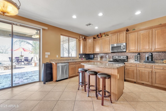 kitchen with light stone countertops, a center island, visible vents, appliances with stainless steel finishes, and decorative backsplash