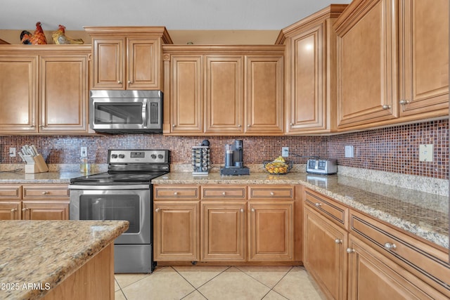 kitchen featuring stainless steel appliances, decorative backsplash, light stone counters, and light tile patterned floors