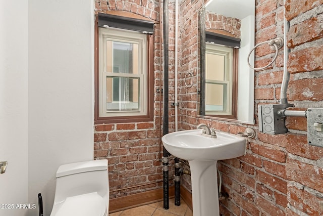 bathroom featuring tile patterned flooring, a sink, brick wall, and toilet