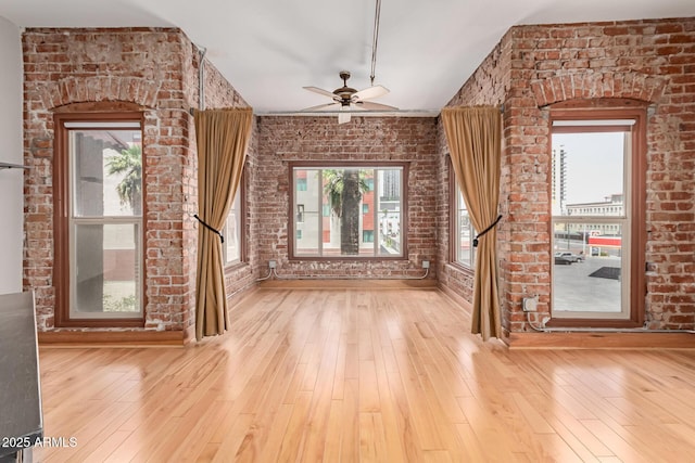 unfurnished living room featuring wood-type flooring, ceiling fan, and brick wall