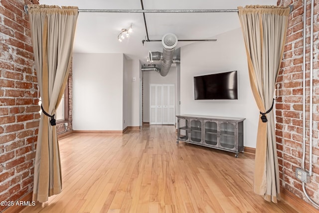 unfurnished living room with baseboards, wood-type flooring, and brick wall