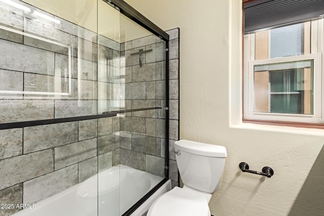 bathroom featuring toilet and shower / bath combination with glass door