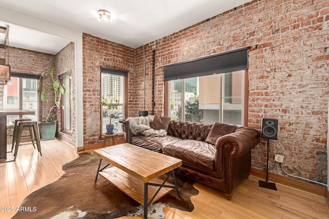 living area with plenty of natural light, brick wall, and hardwood / wood-style flooring