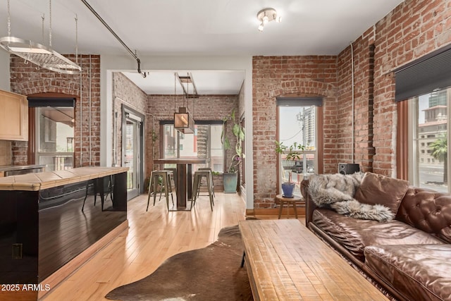 living area featuring wood-type flooring, brick wall, and plenty of natural light