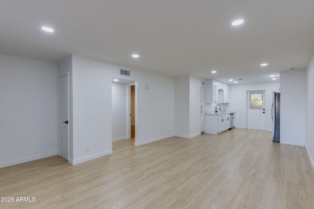 unfurnished living room with a sink, recessed lighting, light wood-type flooring, and baseboards