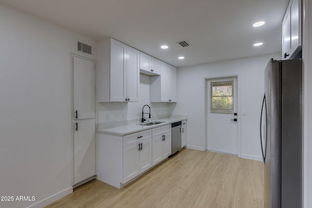 kitchen featuring stainless steel appliances, a sink, light wood finished floors, white cabinetry, and recessed lighting
