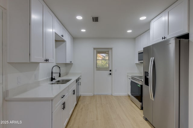 kitchen featuring stainless steel appliances, a sink, light wood-style floors, light countertops, and baseboards