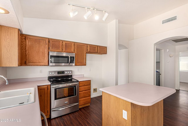 kitchen featuring a sink, appliances with stainless steel finishes, dark wood finished floors, brown cabinets, and arched walkways