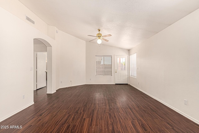 empty room featuring arched walkways, dark wood-style floors, ceiling fan, and visible vents