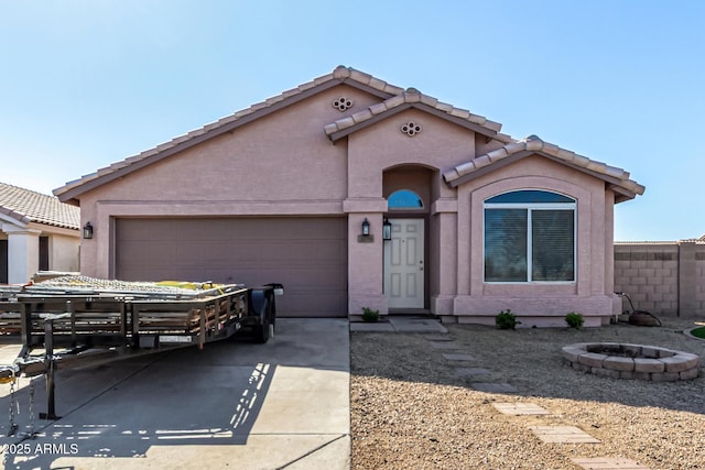 mediterranean / spanish-style house featuring stucco siding, fence, driveway, a fire pit, and a garage