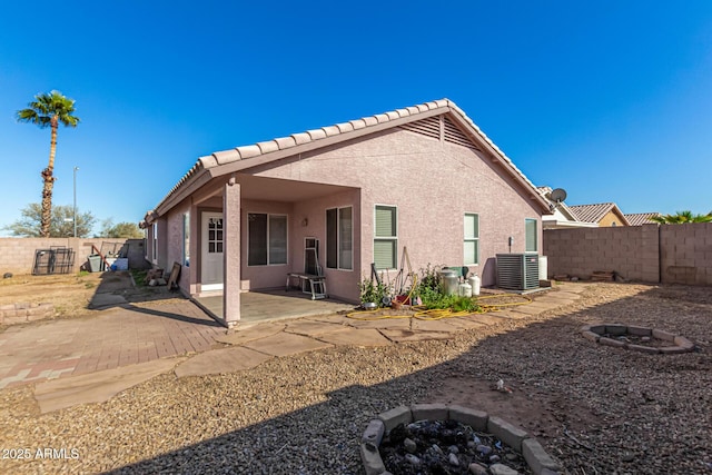 rear view of property featuring a fire pit, cooling unit, stucco siding, a fenced backyard, and a tiled roof