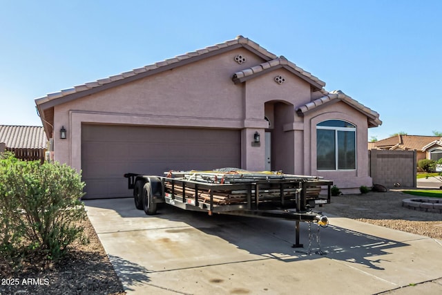 mediterranean / spanish house with concrete driveway, stucco siding, fence, a tiled roof, and a garage