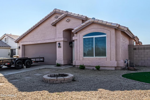 mediterranean / spanish-style house with stucco siding, fence, driveway, an outdoor fire pit, and a garage