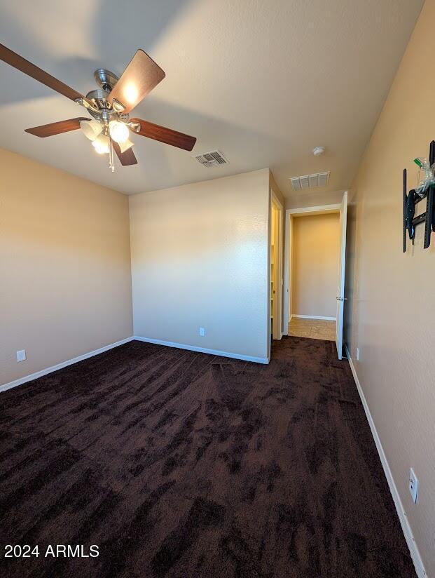 empty room with ceiling fan and dark colored carpet