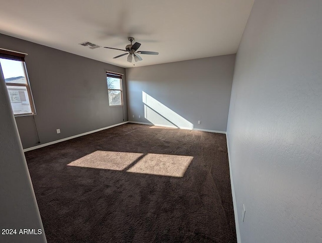 empty room with ceiling fan and dark colored carpet