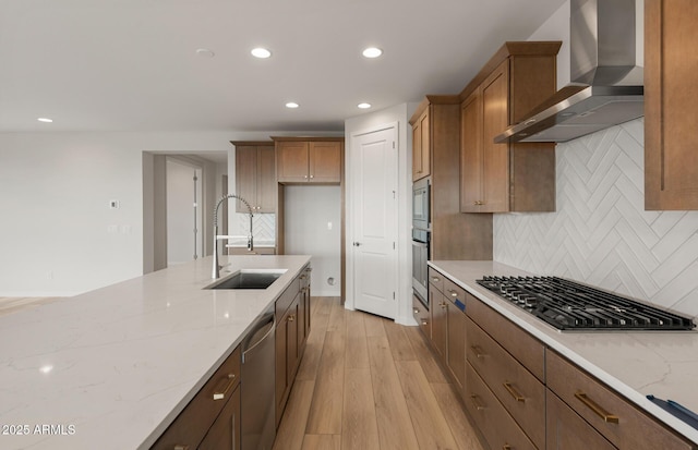 kitchen featuring stainless steel appliances, light stone countertops, sink, and wall chimney range hood