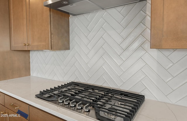 interior details with light stone countertops, stainless steel gas cooktop, wall chimney range hood, and decorative backsplash