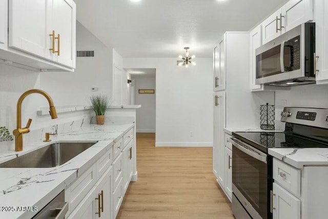 kitchen featuring light wood-type flooring, light stone counters, stainless steel appliances, sink, and white cabinetry