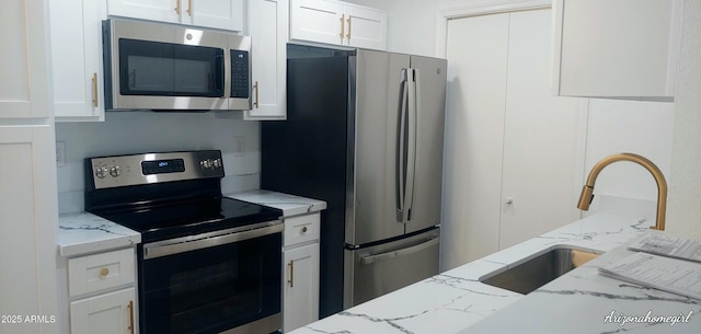 kitchen with light stone countertops, white cabinetry, sink, and stainless steel appliances