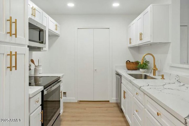 kitchen with light stone countertops, appliances with stainless steel finishes, sink, light hardwood / wood-style flooring, and white cabinets