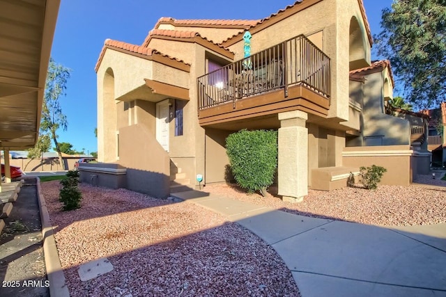 exterior space with a balcony, a tile roof, and stucco siding