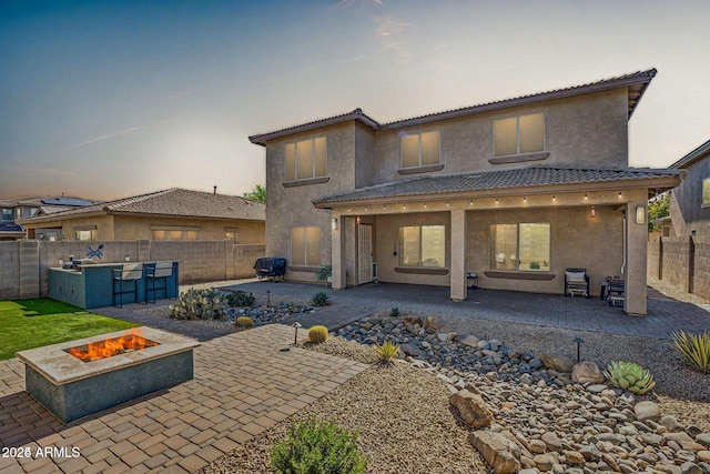 back of property featuring a fire pit, a fenced backyard, a tiled roof, a patio area, and stucco siding