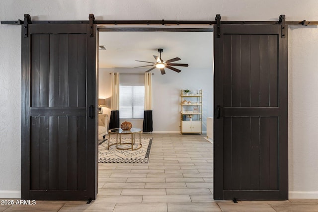 sitting room with a barn door, wood finish floors, a ceiling fan, and baseboards