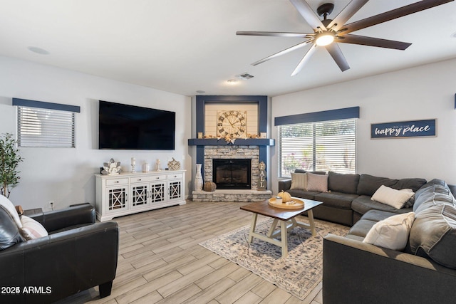 living room featuring a ceiling fan, light wood-type flooring, visible vents, and a fireplace